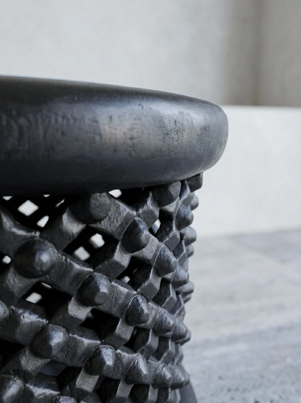 Detail van met de hand gebeitelde knopen en mat gezwart patina op de sculpturale kruk